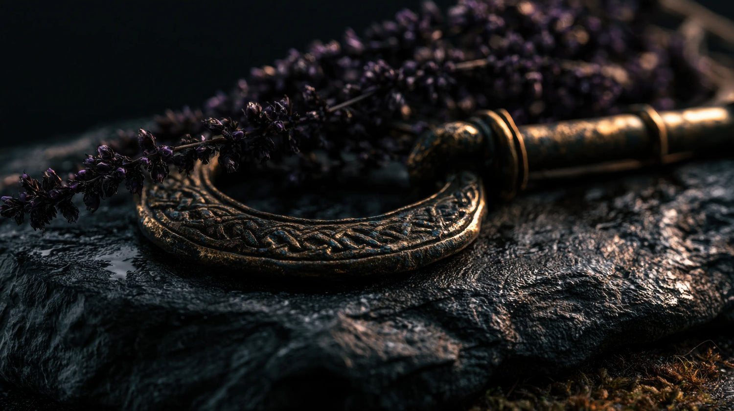 A dramatic, close-up macro photograph featuring an ancient, heavy bronze ring adorned with intricate Celtic knotwork, resting on a slab of dark, wet, deeply textured stone. Beside the antique hardware lies a delicate, dried sprig of dark purple heather. The moody, atmospheric lighting highlights the rich patina of the metal and the rugged environment, perfectly capturing the ancient lore and enduring English heritage that inspires Caracoda Equestrian's traditional craftsmanship.
