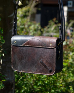 Back view of Oddity No. II, a unique two-tone repurposed saddle leather crossbody bag, resting in a natural outdoor setting.
